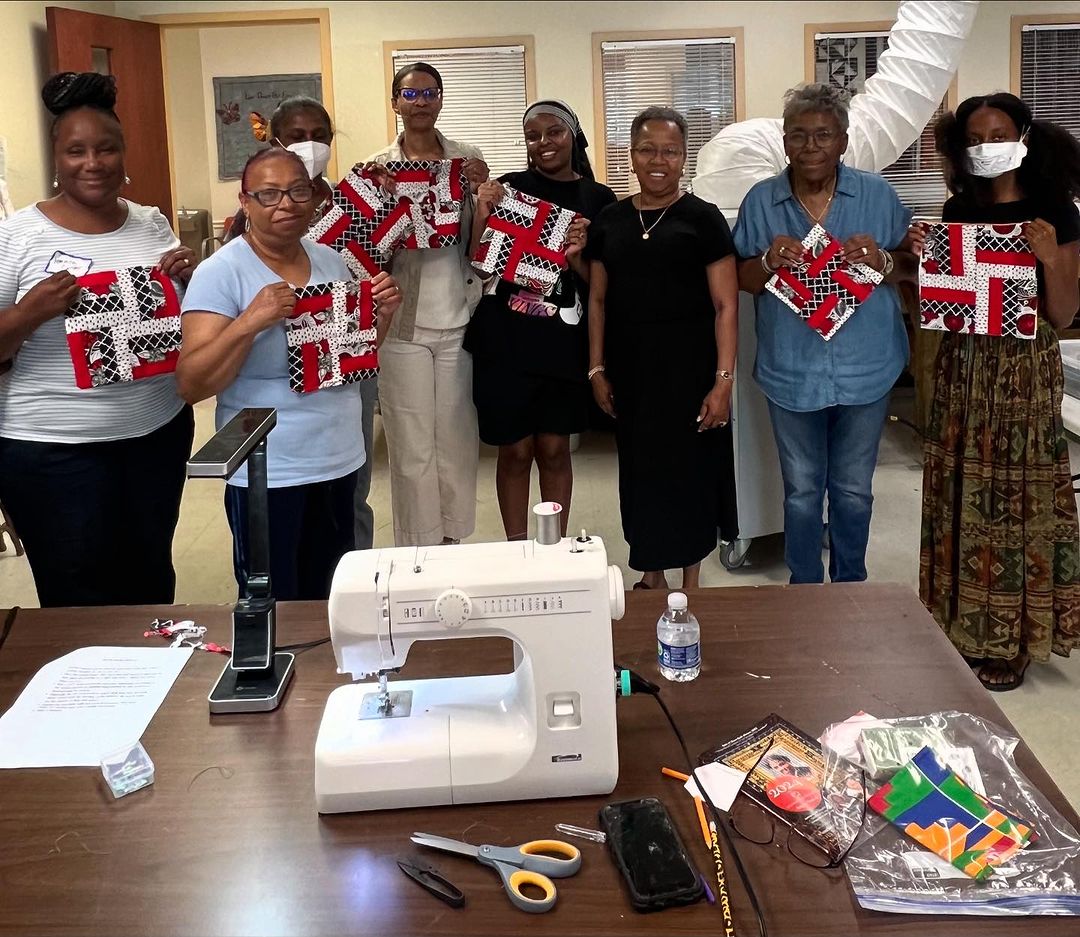 A group of Black women showcasing red, black, and white quilt blocks