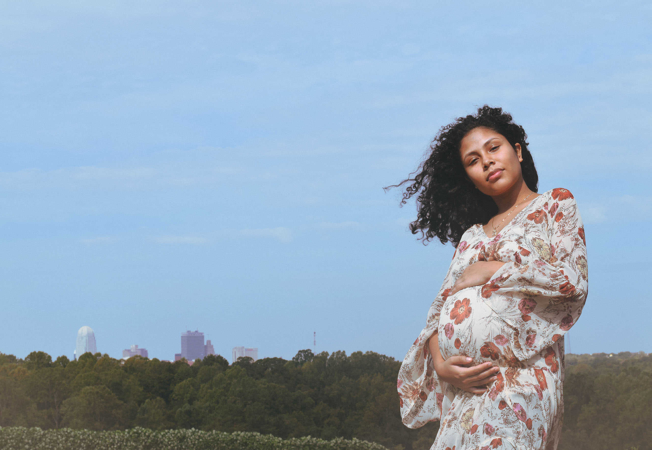 A woman with curly hair poses while holding her pregnant belly